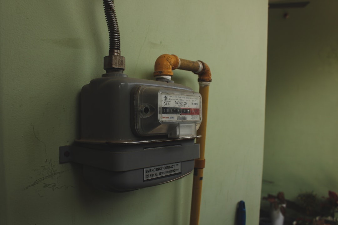 Gray domestic gas meter mounted on a green wall.